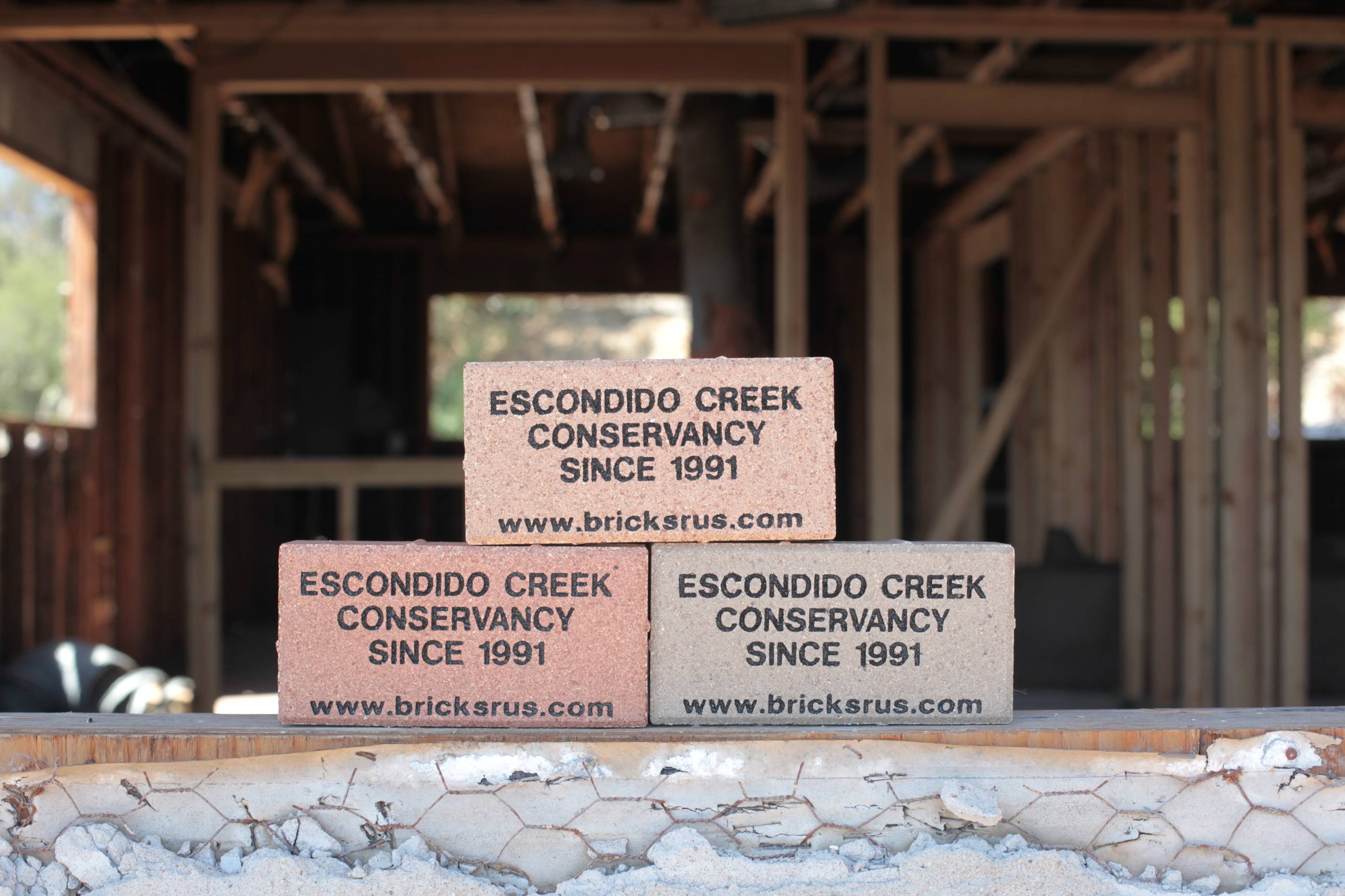 A stack of example bricks to show what a custom memorial brick purchase would look like with text on them. Sitting on a window sill with a framed out room in the background.