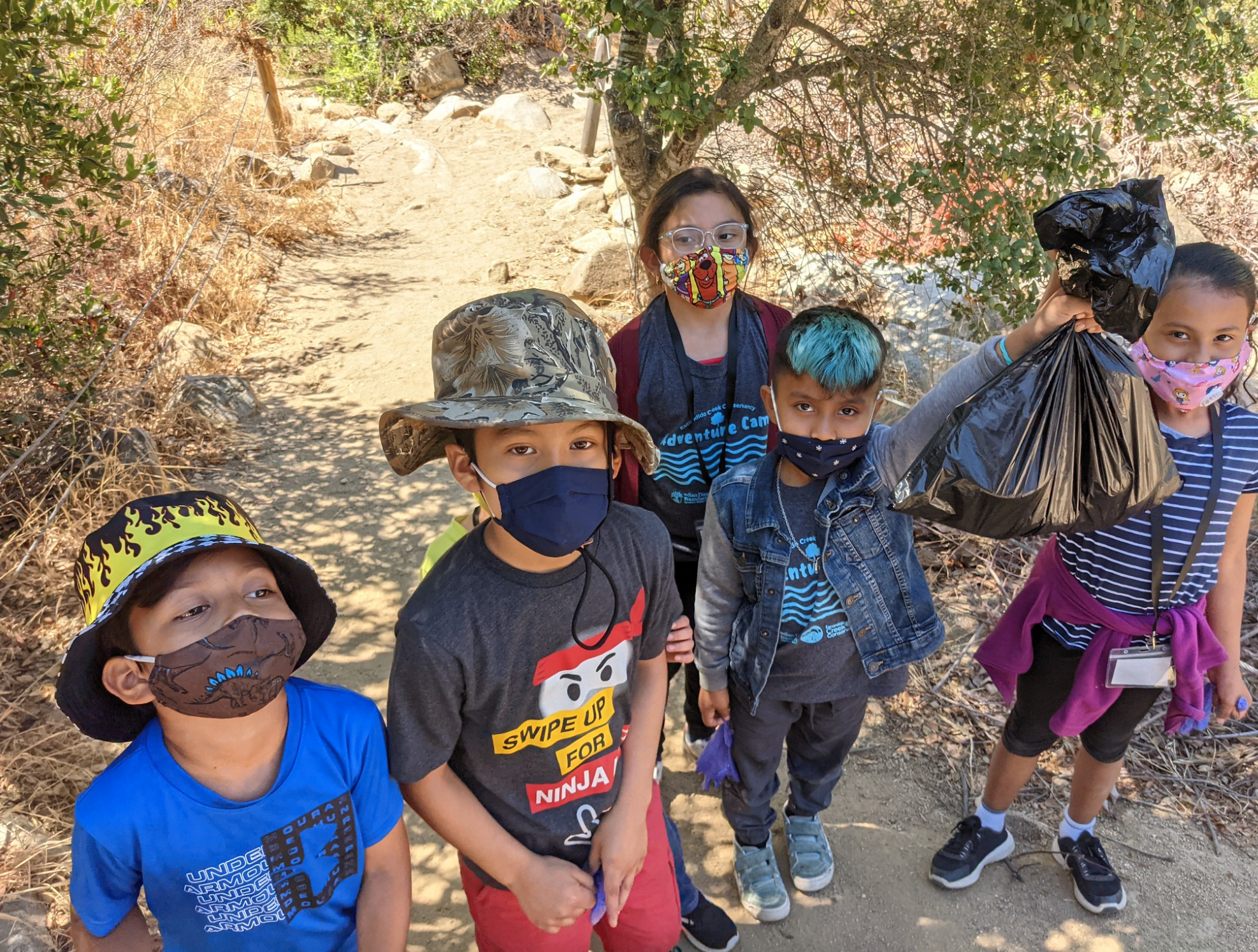 Five elementary students hold up their bags of recycling collected from a local nature preserve.