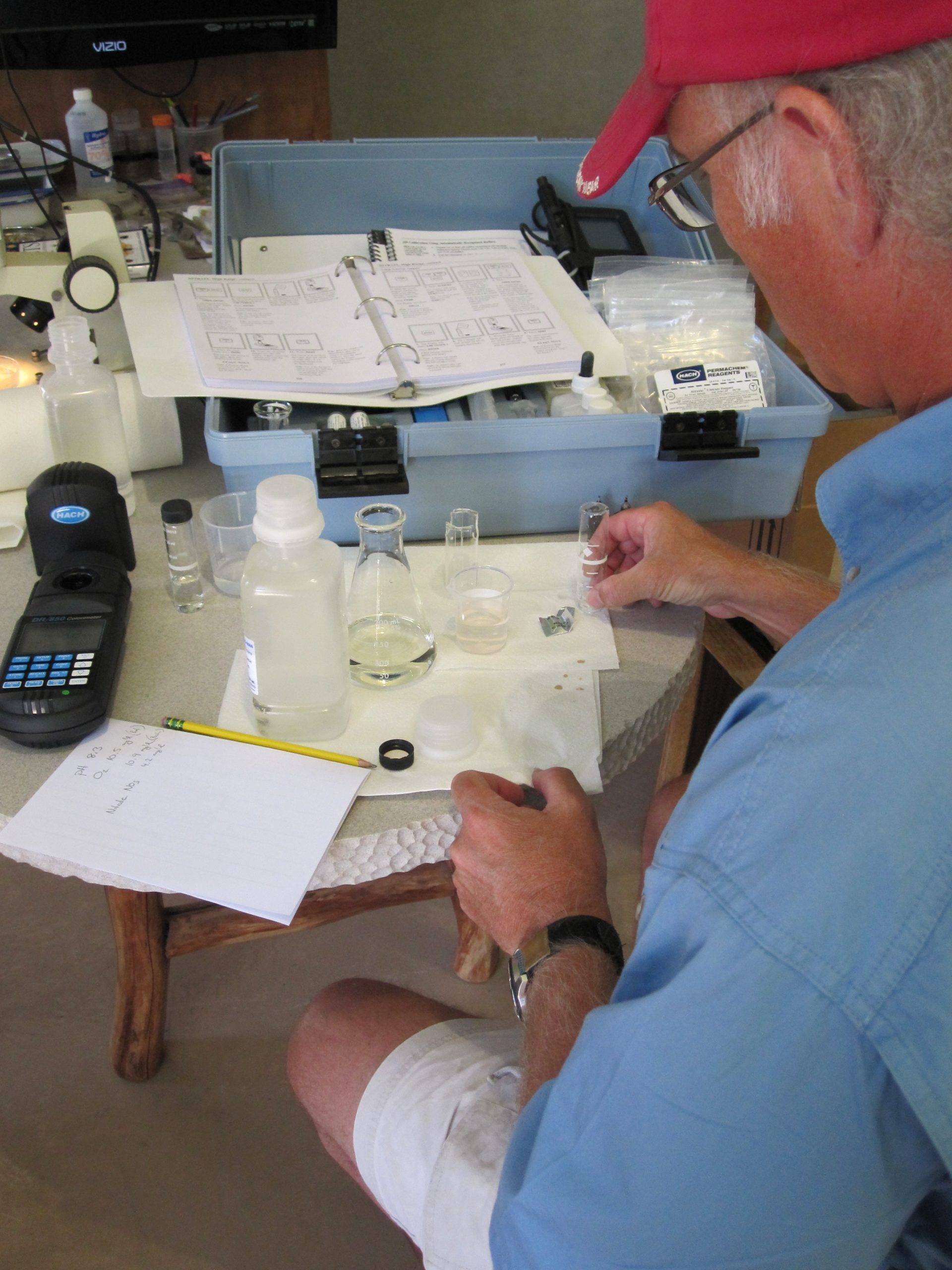 A man making notes at a table filled with water quality samples. Photo shot from over his shoulder.