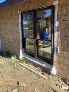A close up of the outside of an under construction ranch home, focused on a new floor to ceiling window being inserted.