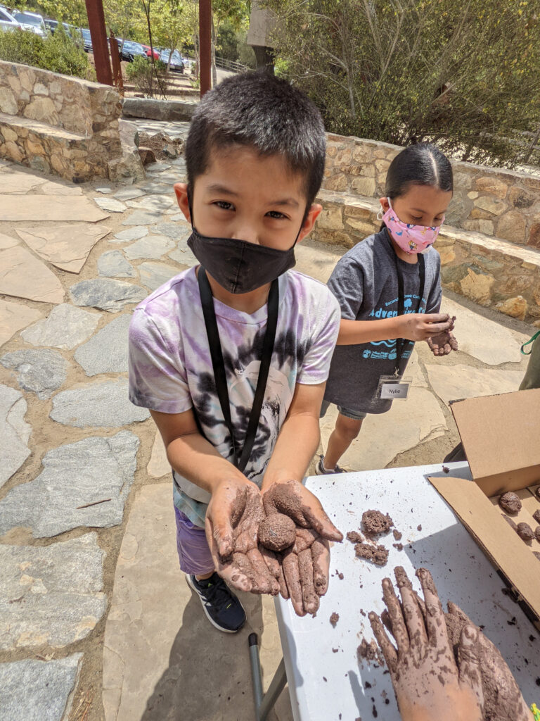 An elementary students uses both hands to hold owl droppings up to the camera during summer Adventure Camp.
