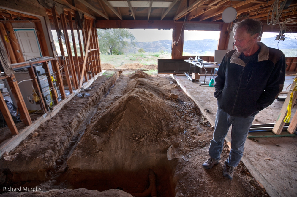 Kevin Barnard looks down at a trench dug for pipes inside a 2x4 framed office space.