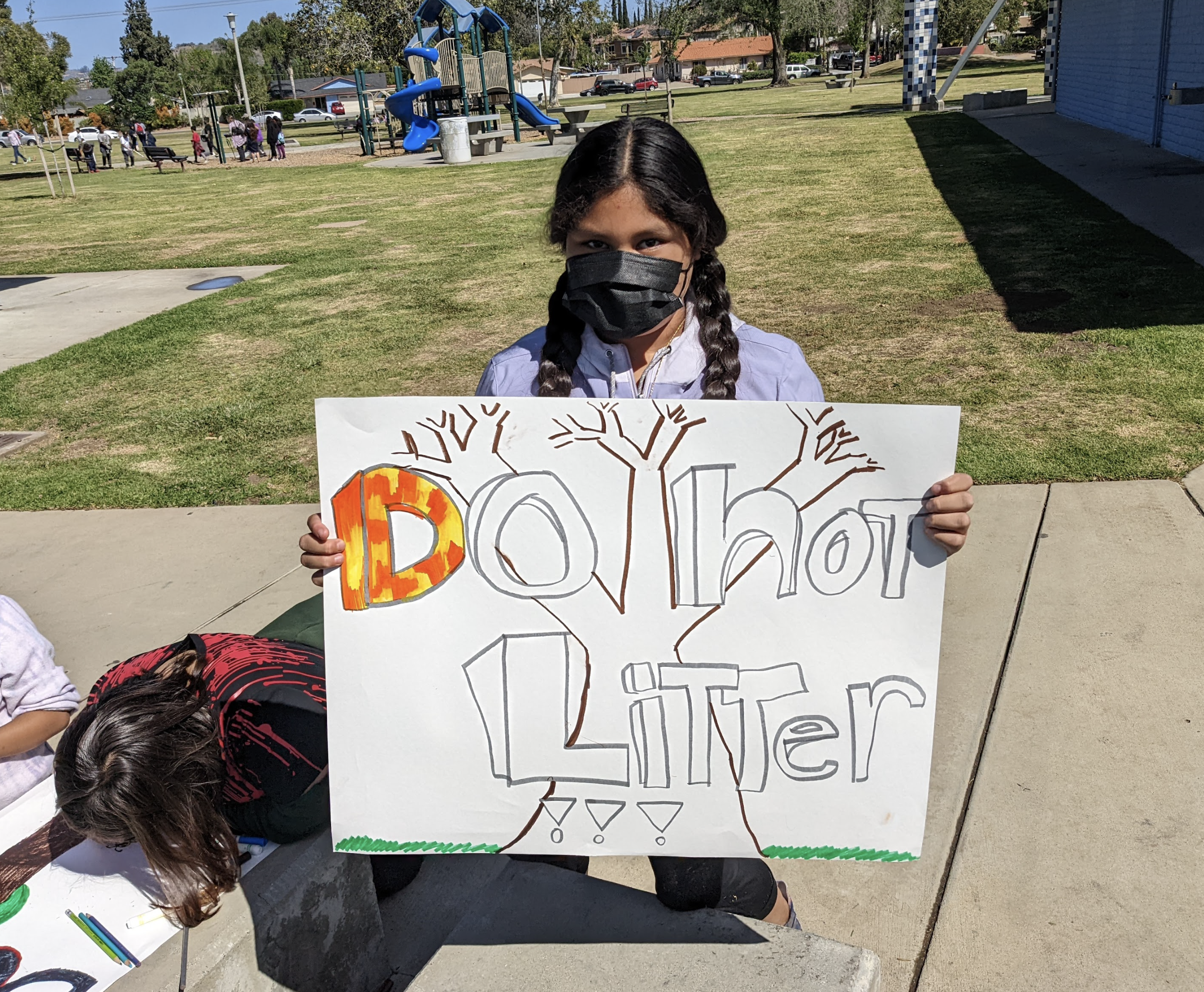 An elementary student holds up a sign decrying litter in a local park.
