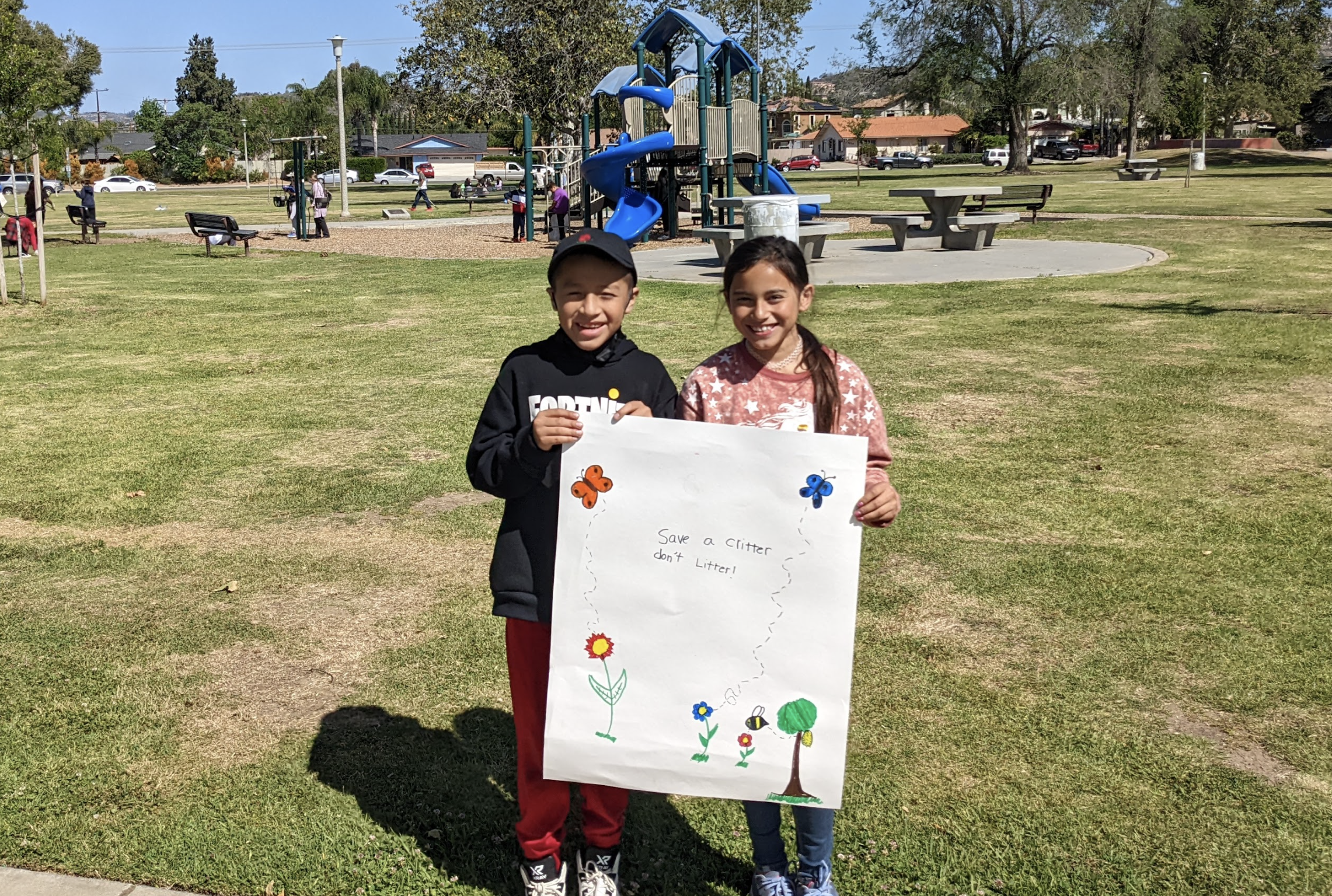 A pair of students hold up an Earth Day sign while in the park.
