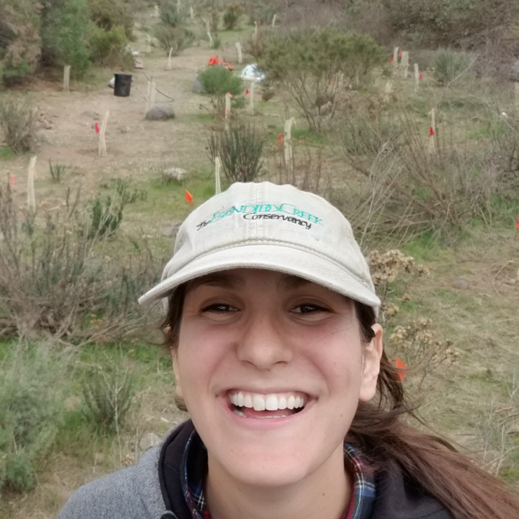 Hannah smiles directly into the camera with native plants in the background